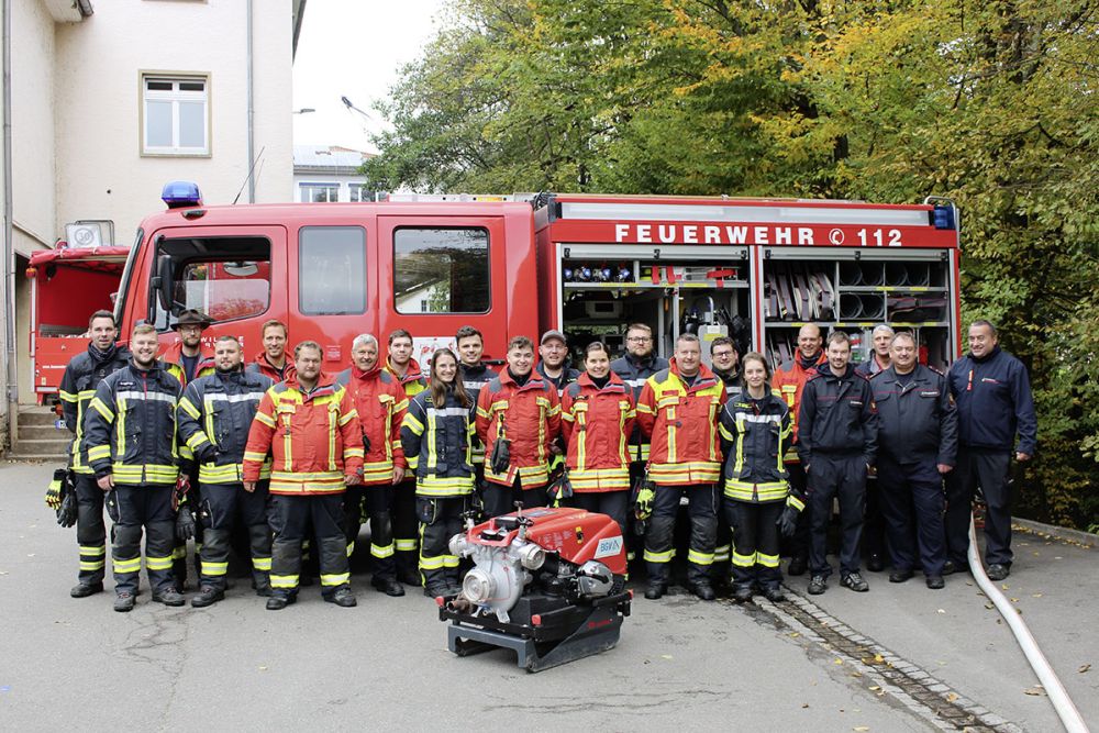 Absolventen und Absolventinnen des Maschinistenlehrgangs in Mosbach. Sie stehen vor einem Feuerwehrauto, vor ihnen steht eine Pumpe.